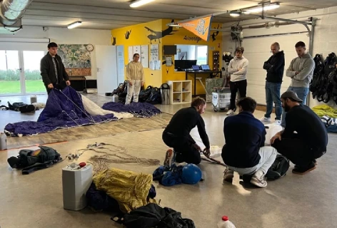 Moniteur fédéral explique le pliage du parachute à plusieurs élèves en salle de pliage.